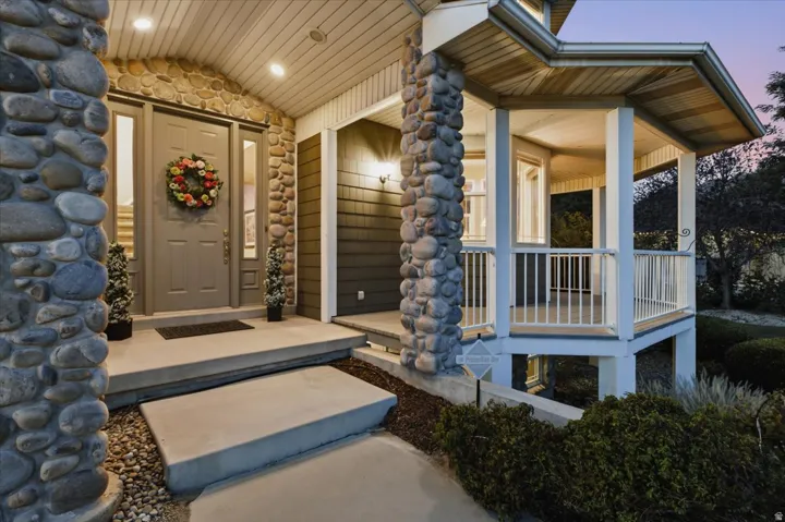 Stone-clad entrance with a solid panel door, sidelight windows, and an adjacent covered porch featuring white railings