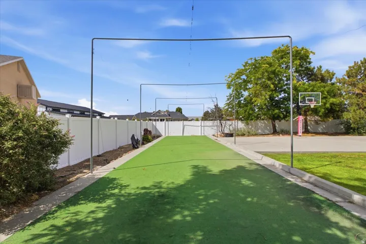 Expansive artificial turf area with perimeter fencing, metal support structures, and a partial basketball court