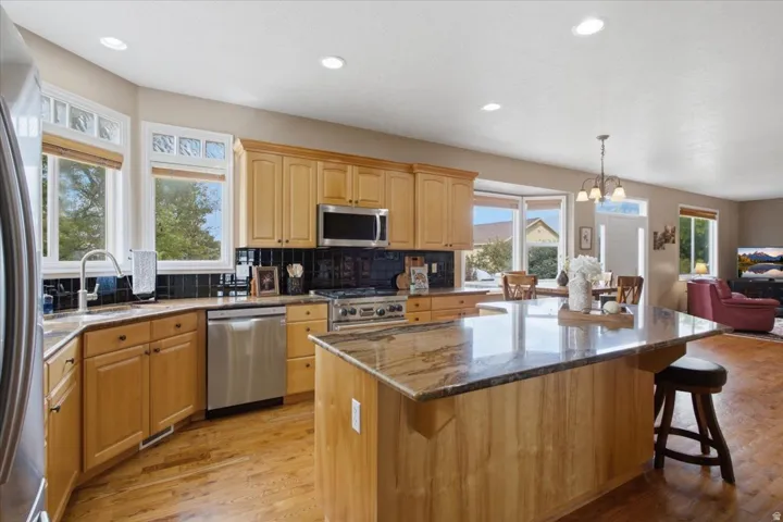 Kitchen featuring wood cabinetry, stainless steel appliances, a dark tile backsplash, and an island with a stone countertop