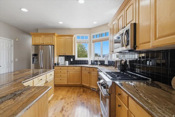 Kitchen featuring wood cabinetry, stainless steel appliances, dark tile backsplash, and light-toned wood-finish flooring