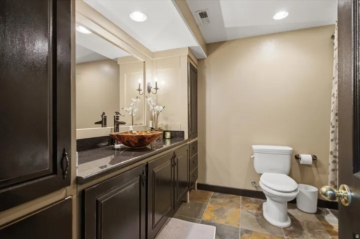Extended vanity with dark cabinetry, stone-finish countertop, and vessel sink