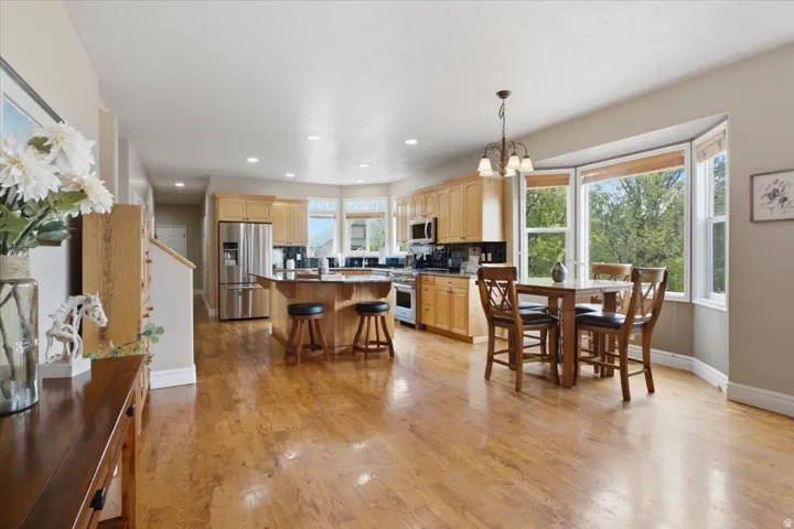 Open-concept living space with wood-finish flooring, a kitchen island with seating, stainless steel appliances, and a dining area with a bay window