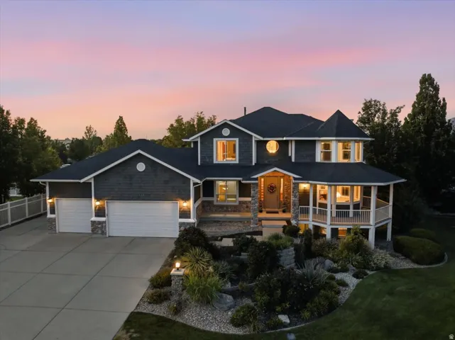 Two-story residence featuring a turret accent, stone facade elements, a multi-car garage, an elevated covered porch, and landscaped grounds
