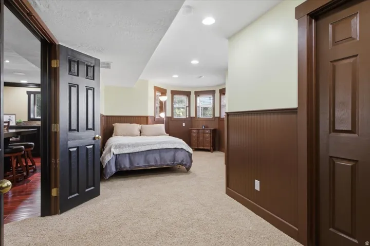 Recessed lighting, warm wood-finish wainscoting, beige carpeting, and a bay window