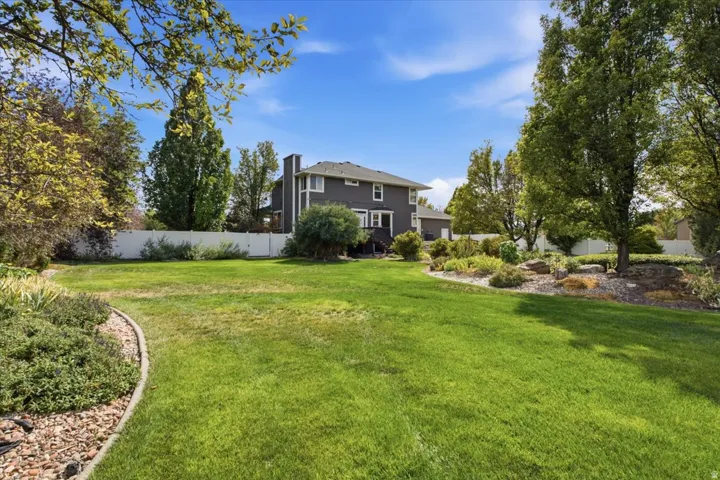 Expansive backyard featuring a manicured lawn, established landscaping, mature trees, and a white perimeter fence