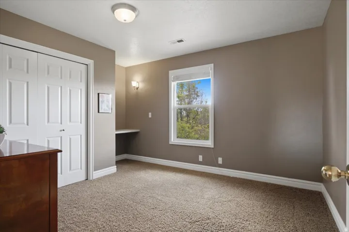 Built-in desk, double closet with paneled bifold doors, window with exterior scenery, wall-mounted sconce, and recessed ceiling light