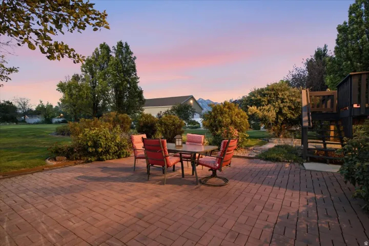 Brick paver patio with a manicured lawn, established landscaping, and a multi-level deck