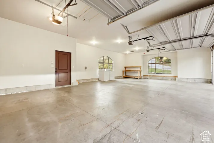 Spacious garage featuring concrete flooring, multiple overhead lights, two arched windows, and an interior door