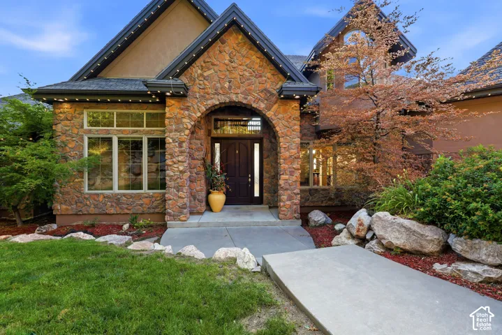 Stone facade with arched entryway, dark wood double front doors, multi-pane windows, and concrete walkways