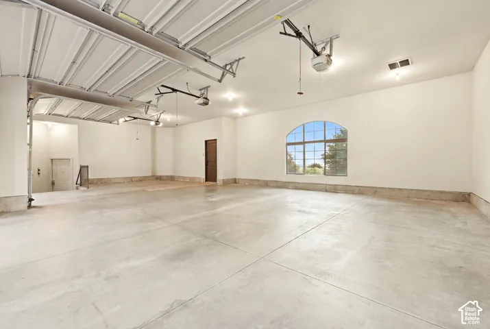 Spacious garage with multiple overhead doors, concrete flooring, arched window, and recessed lighting