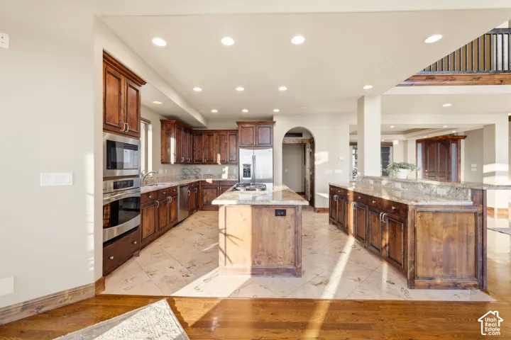 Spacious kitchen featuring rich wood cabinetry, stainless steel appliances, a central island, and stone countertops
