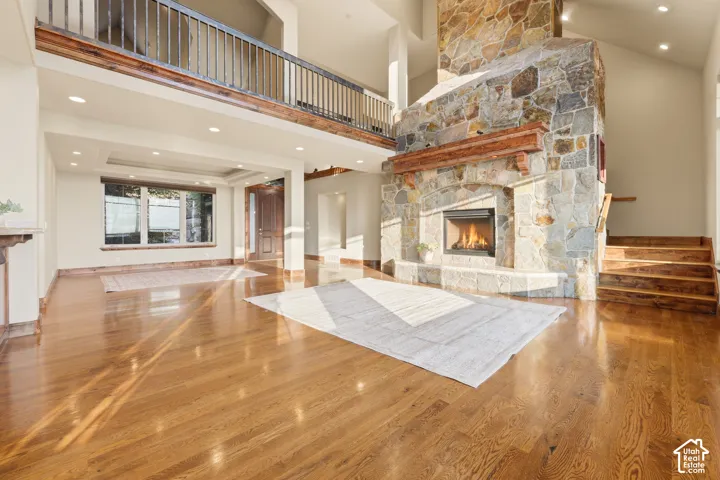 Two-story great room featuring a stone fireplace with a wood-beam mantel, hardwood flooring, and an open balcony with an iron railing