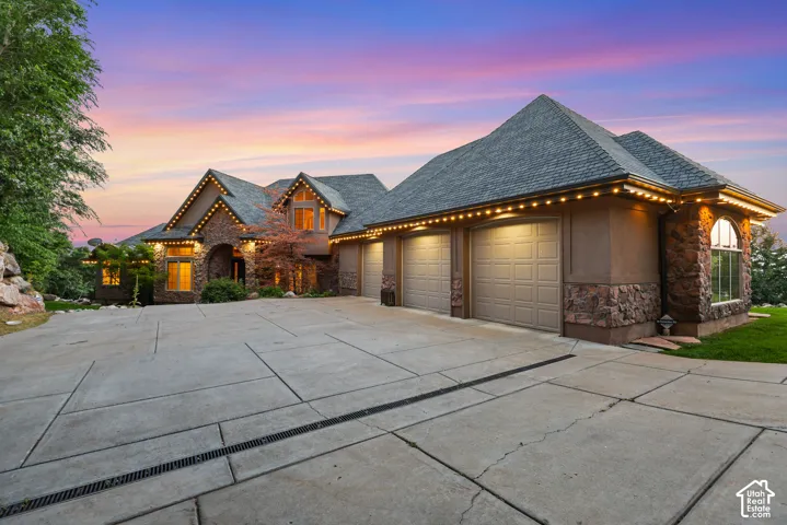 Stone and stucco exterior with a multi-car garage, pitched shingle roof, and expansive concrete driveway