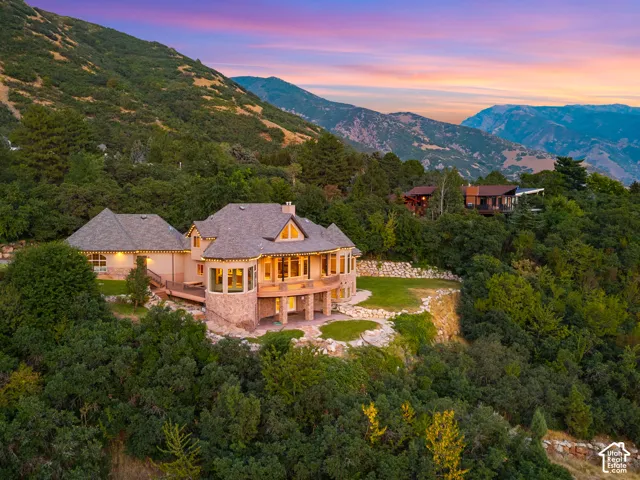 Architectural residence featuring a stone and stucco exterior, multiple balconies, a curved bay window, and a tiered landscaped yard