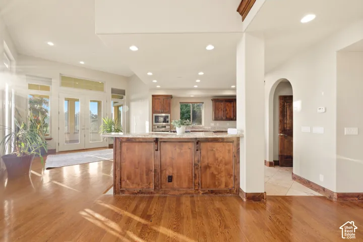 Hardwood flooring, recessed lighting, a kitchen island with storage, double French doors, and an arched doorway