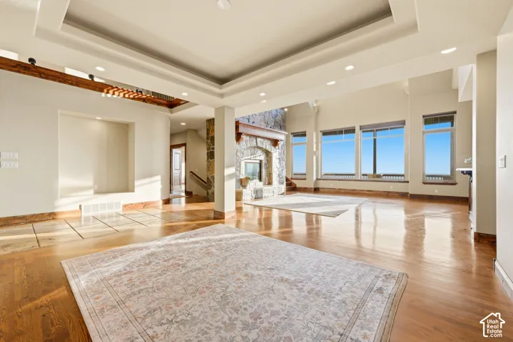 Expansive living area featuring wood-finish flooring, a stone-clad fireplace, large windows, and a coffered ceiling with recessed lighting