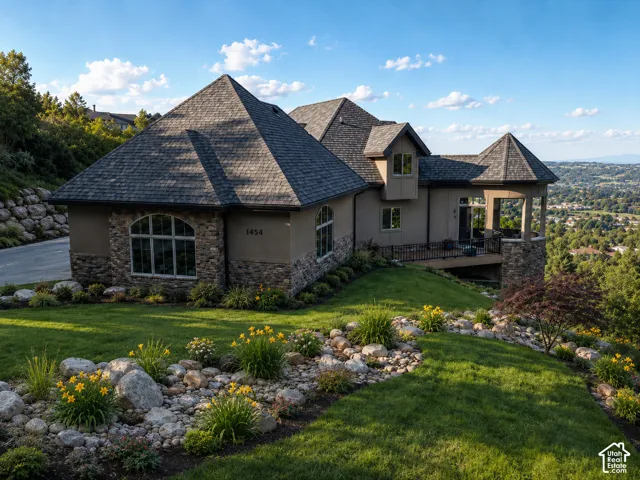 Stone and stucco exterior with an arched window, multi-pitch shingle roof, and a wood-finish deck with a stone column