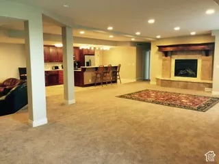 Spacious lower-level living area with recessed lighting, a built-in fireplace with stone surround and wood mantel, and a kitchen area featuring wood cabinetry and a peninsula with seating