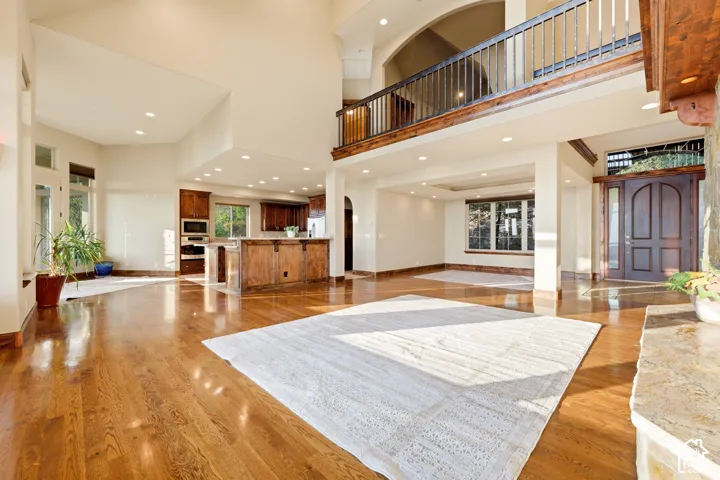 Open concept living area featuring wood-finish flooring, a two-story ceiling, and an upper-level balcony with wood and metal railing