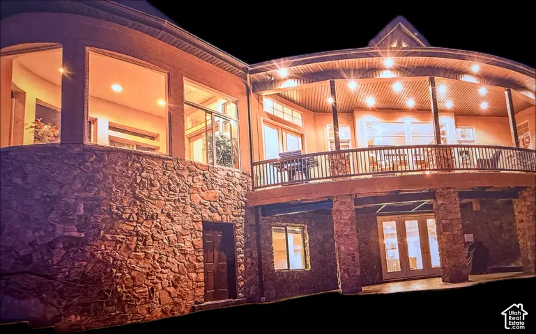 Multi-level exterior with extensive stone masonry, a curved balcony featuring a wood-finish ceiling, and multiple glass doors