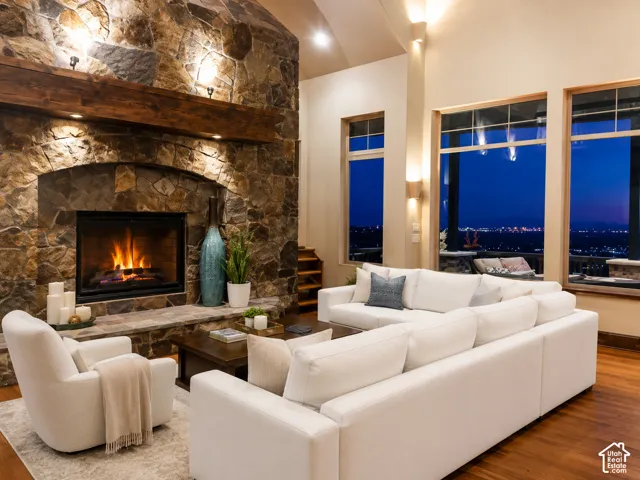 Vaulted ceiling living room featuring a stone-clad fireplace with a wood mantel, wood-finish flooring, and expansive windows