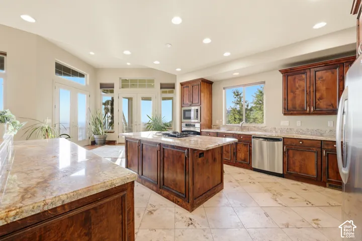 Kitchen featuring wood cabinetry, stainless steel appliances, granite countertops, a center island, and tile flooring