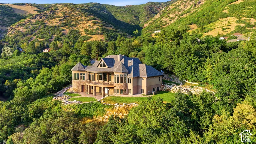 Stone and stucco exterior, multiple gables, extensive window placement, upper-level balcony, and surrounding mature trees