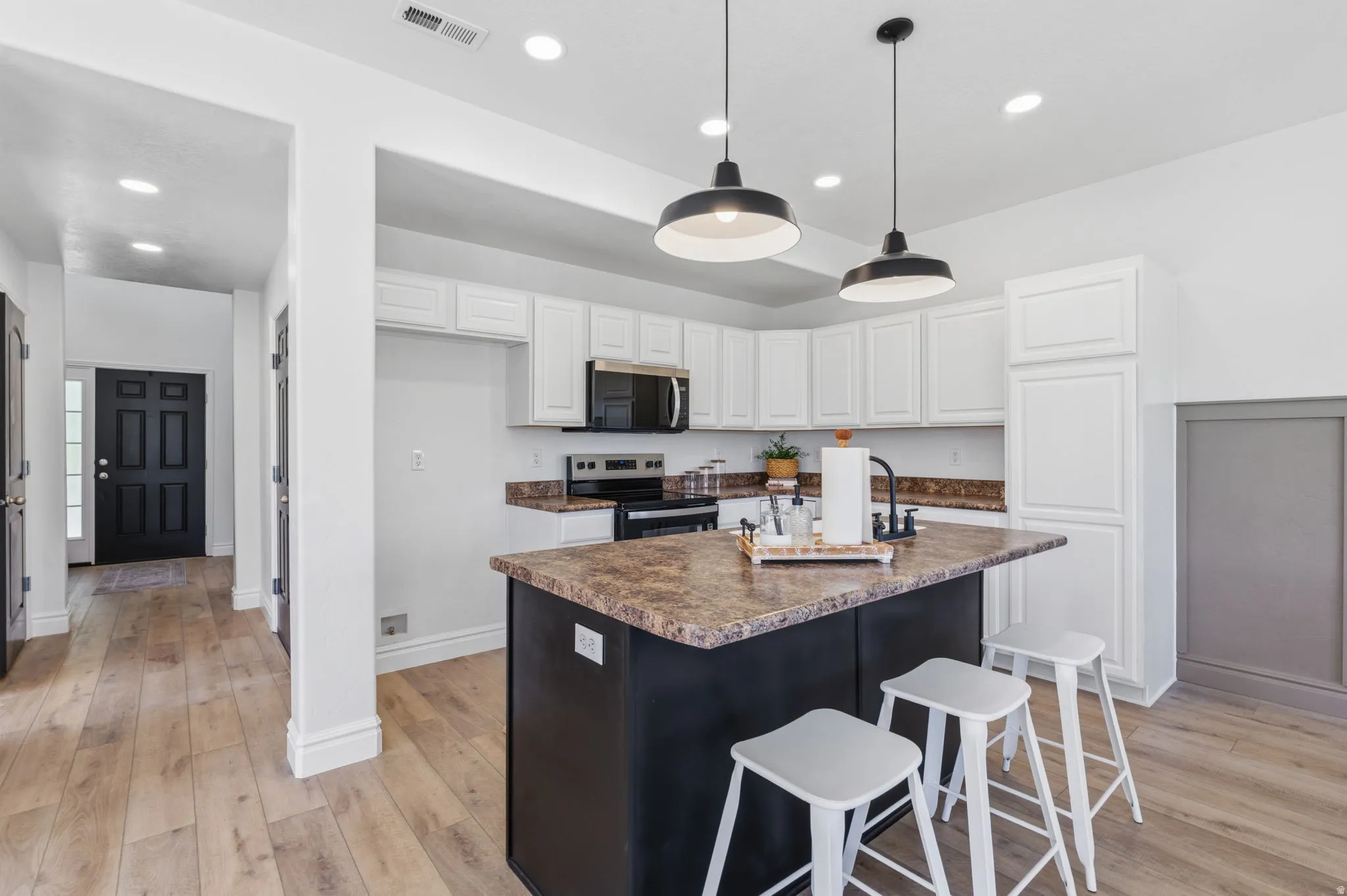Kitchen featuring a central island with a sink, white cabinetry, dark countertops, and wood-finish flooring