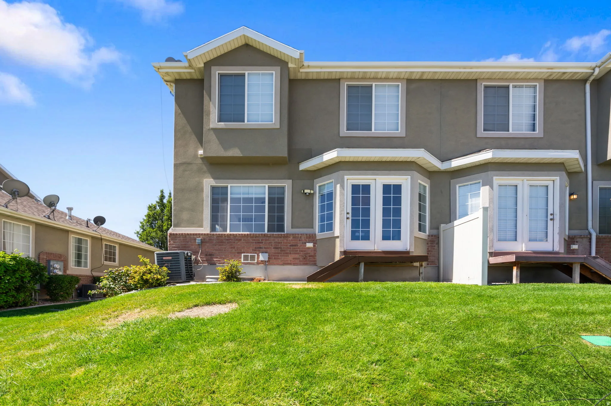 Exterior featuring a multi-level design, multiple windows, double French doors, and a lower-level brick facade