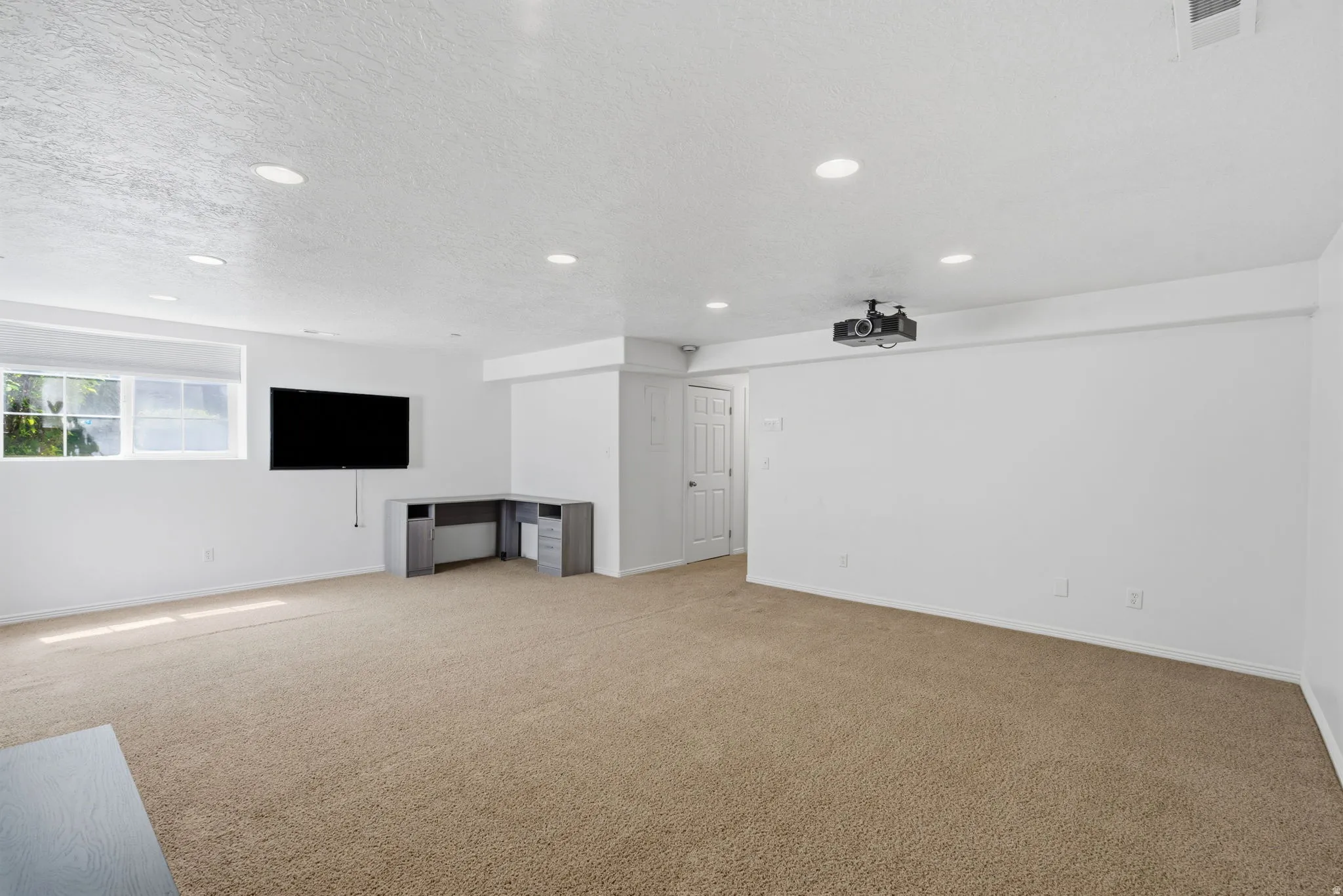 Recessed lighting illuminates this expansive carpeted room with multiple windows