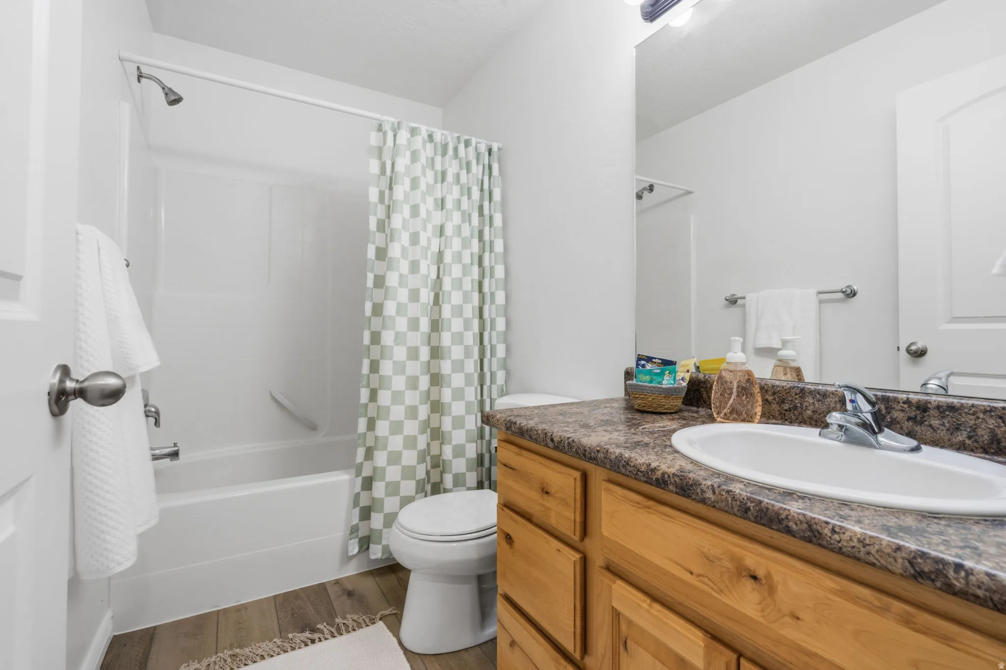 Wood-finish flooring, single vanity with a laminate countertop, and a shower-tub combination