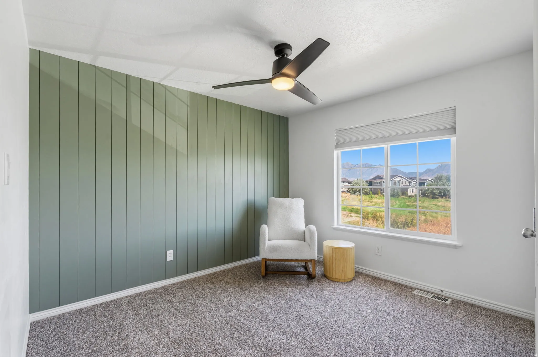 Vertical panel accent wall, window with roller shade, ceiling fan with integrated lighting, wall-to-wall carpeting, and painted walls