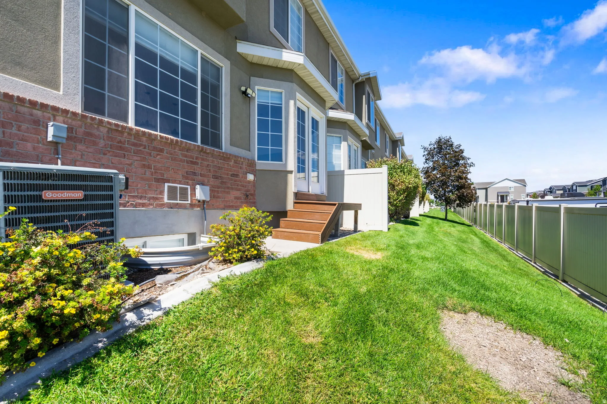 Rear exterior with brick and stucco siding, a ground-level patio door with wood-finish steps, and an expansive lawn area