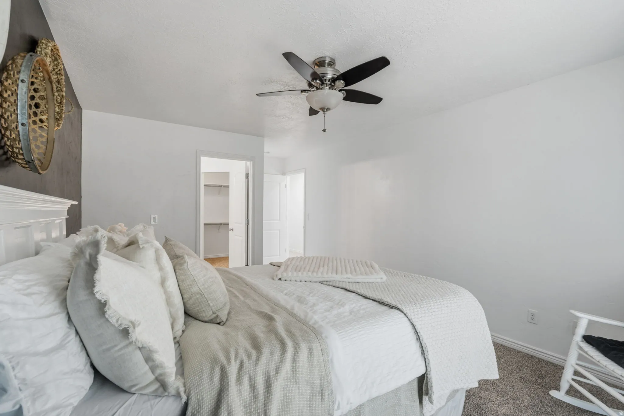 Spacious bedroom with ceiling fan, white paneled headboard, neutral wall finishes, and carpet flooring
