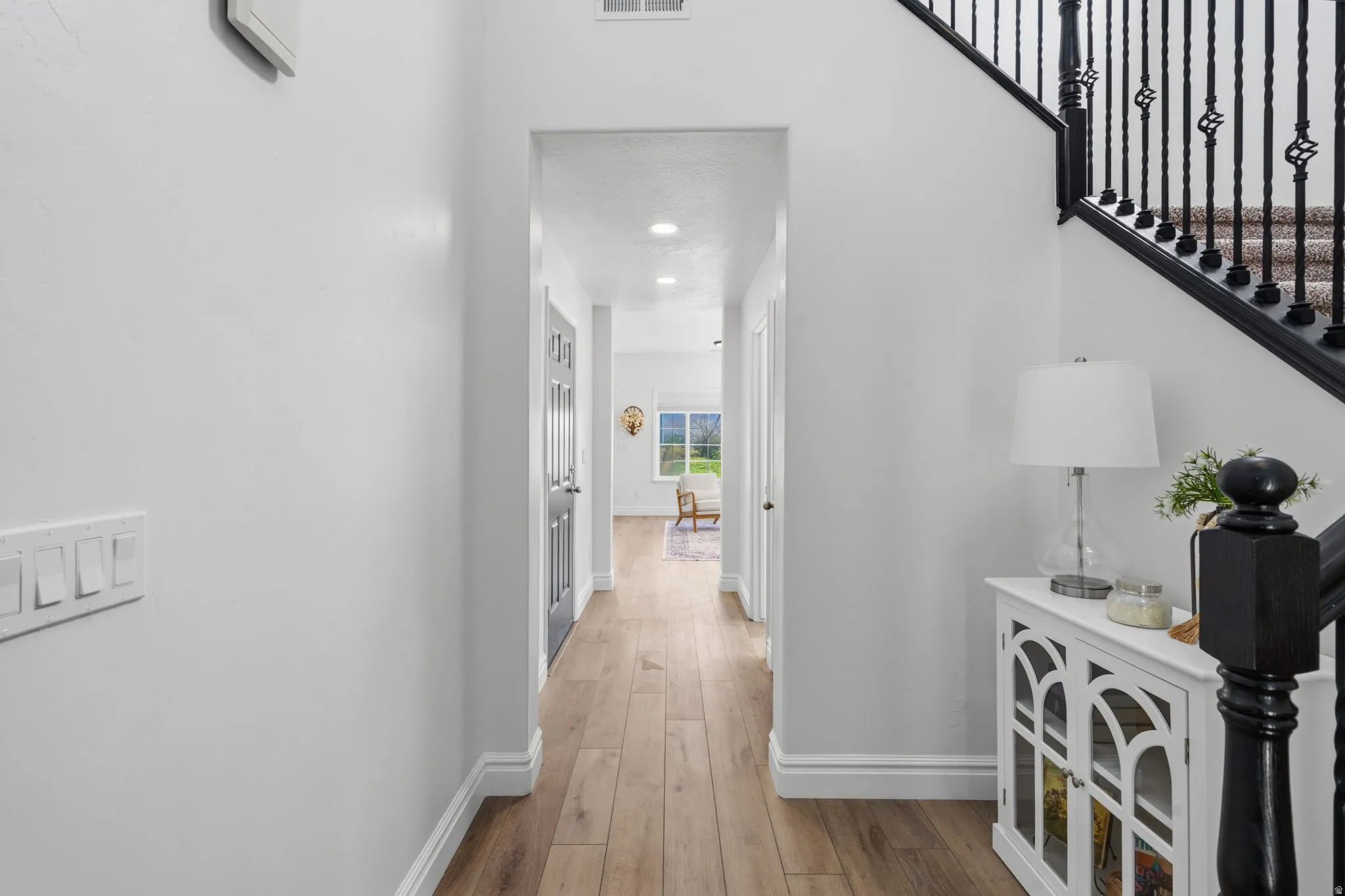 Wood-finish flooring throughout, white baseboards, and a black staircase with decorative iron balusters