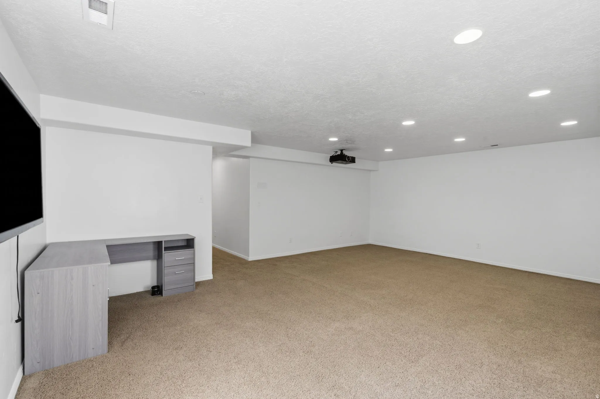 Spacious room featuring neutral carpeting, recessed lighting, and a mounted projector