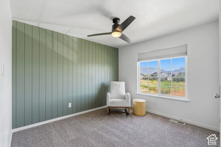 Vertical panel accent wall, window with roller shade, ceiling fan with integrated lighting, wall-to-wall carpeting, and painted walls