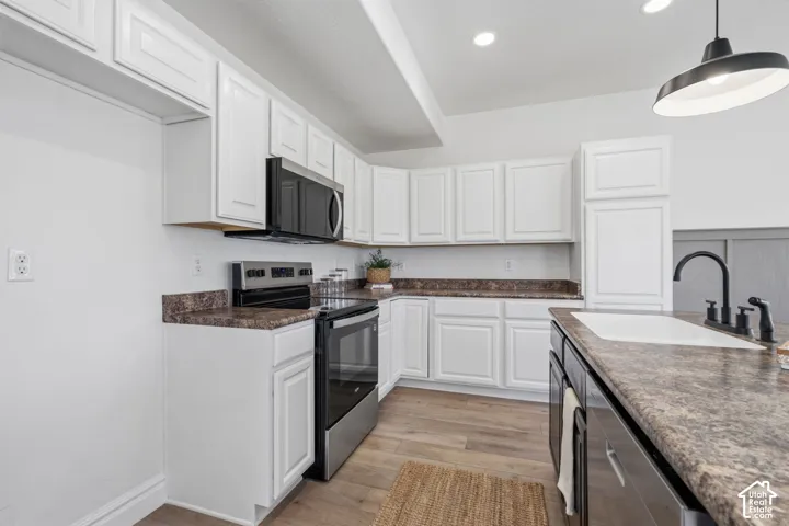 White cabinetry with brushed nickel hardware, stainless steel appliances, wood-finish flooring, recessed lighting, and an island with a white sink and black faucet