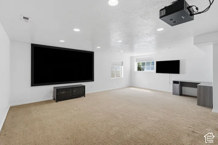 Recessed ceiling lighting, wall-mounted projector, large projection screen, carpet flooring, and multiple windows