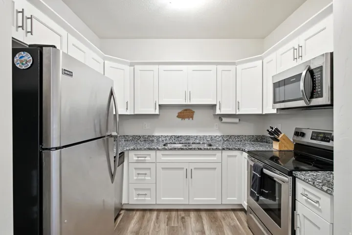 White shaker-style cabinetry, stainless steel appliances, speckled stone countertops, and wood-finish flooring