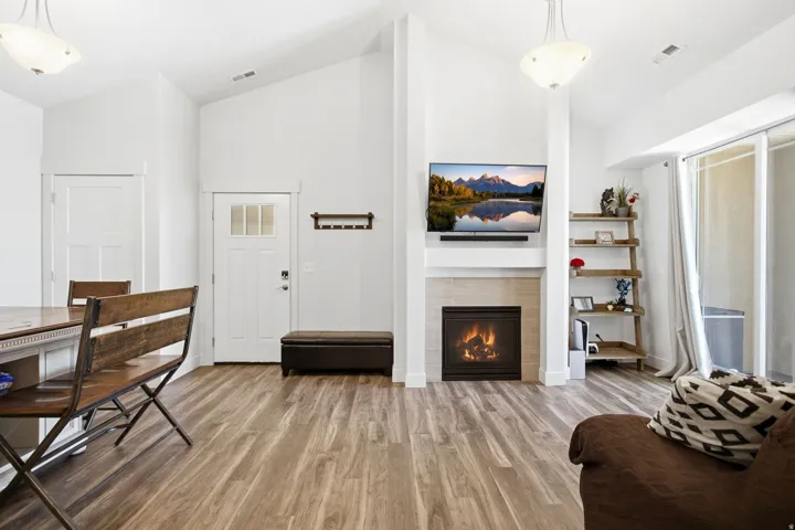 Vaulted ceiling with pendant lighting, wood-finish flooring, fireplace with tiled surround, white paneled doors, and sliding glass door