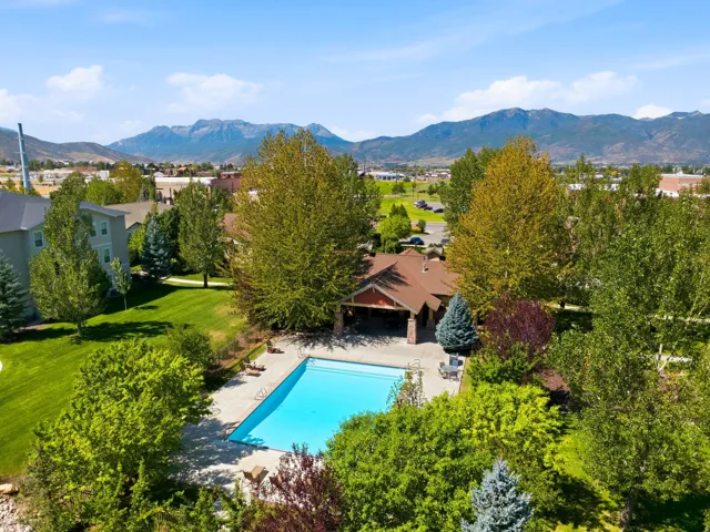 Expansive outdoor pool with a surrounding concrete deck, mature trees, and a clubhouse featuring a covered patio