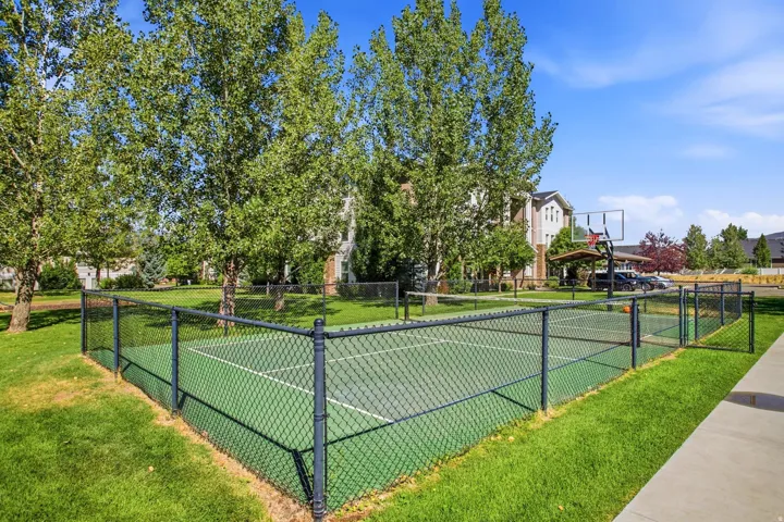 Outdoor sports court with a black chain-link fence, surrounded by mature trees and green lawns
