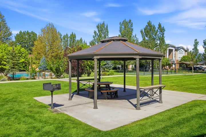 Gazebo with picnic tables, a built-in barbecue grill, surrounding green space, and nearby swimming pool