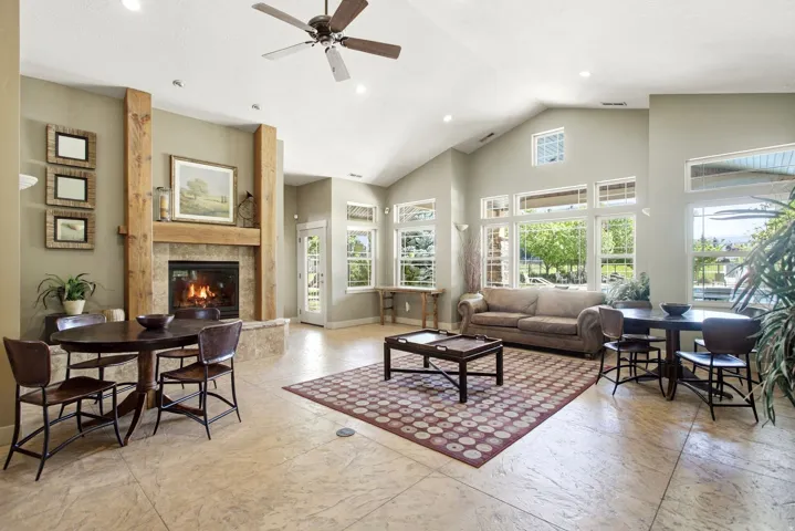 Vaulted ceiling, recessed lighting, ceiling fan, stone fireplace with a wood-finish mantel, and large windows