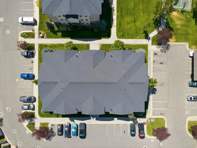 Expansive asphalt parking areas, mature trees, manicured green spaces, and a composite shingle roof