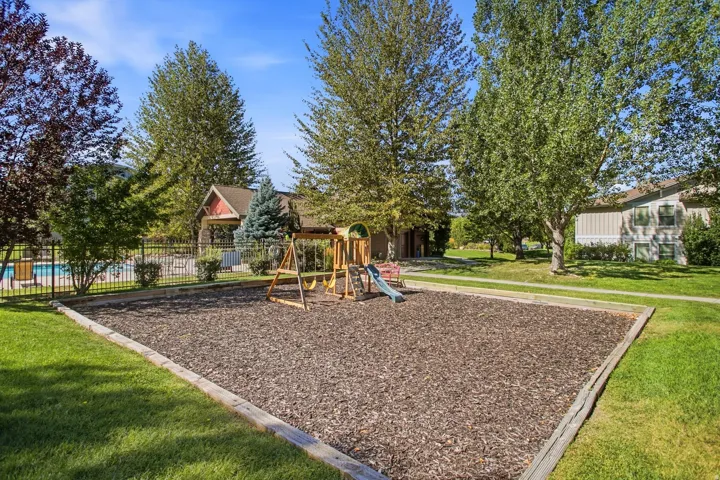 Outdoor playground with wood chip surfacing, green lawn, and mature trees