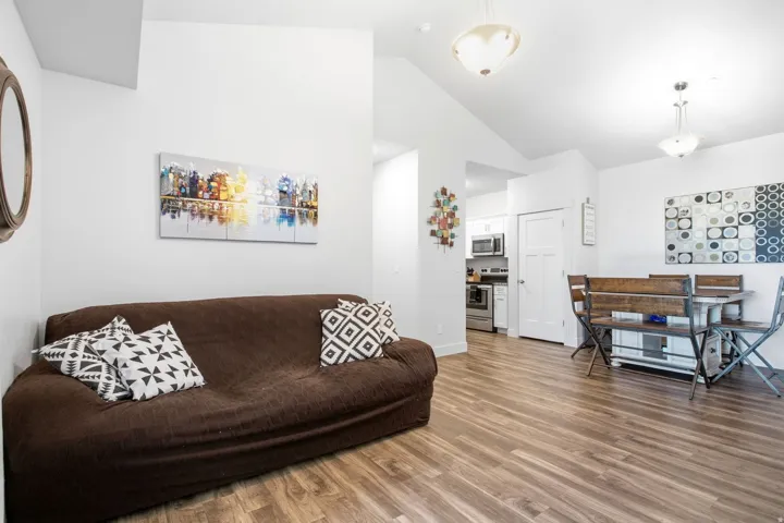Vaulted ceiling with overhead lighting, wood-finish flooring, white painted walls, and white trim