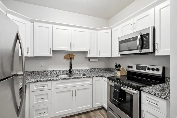 White shaker-style cabinetry, stainless steel appliances, granite-style countertops, wood-finish flooring, and a single-basin sink with a matte black faucet