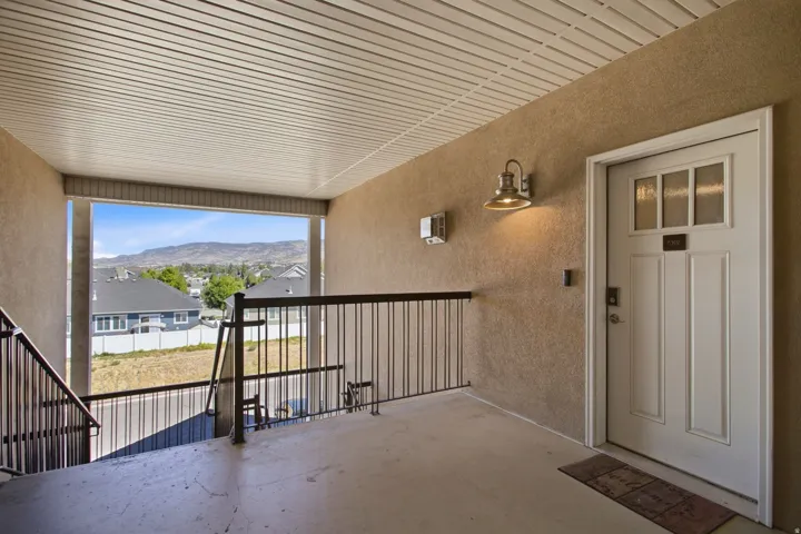 Covered outdoor balcony with mountain scenery, stucco exterior, metal railing, and a white paneled entry door with frosted glass inserts